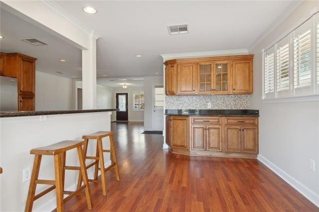 kitchen featuring decorative backsplash, stainless steel fridge, dark hardwood / wood-style floors, a breakfast bar, and crown molding