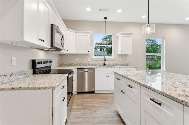 kitchen with white cabinetry, appliances with stainless steel finishes, light stone countertops, pendant lighting, and sink