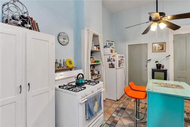 kitchen with a breakfast bar area, ceiling fan, white appliances, tile patterned flooring, and a center island