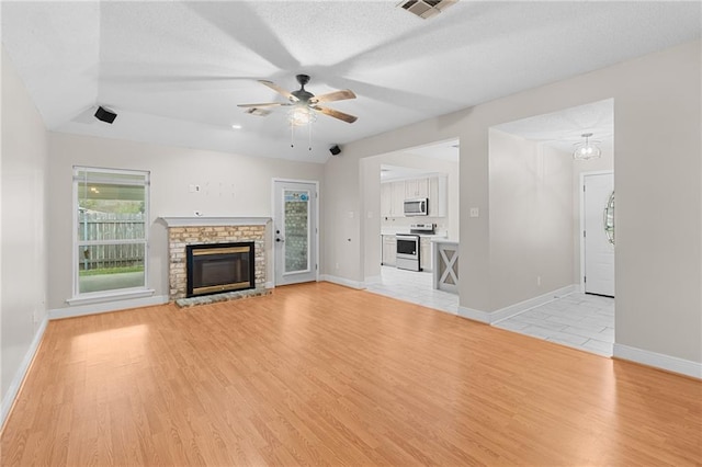 unfurnished living room with ceiling fan, plenty of natural light, a fireplace, and light hardwood / wood-style flooring