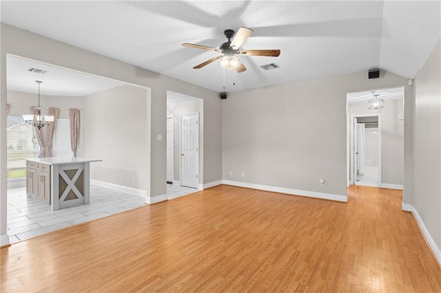 empty room featuring ceiling fan with notable chandelier, vaulted ceiling, and light wood-type flooring