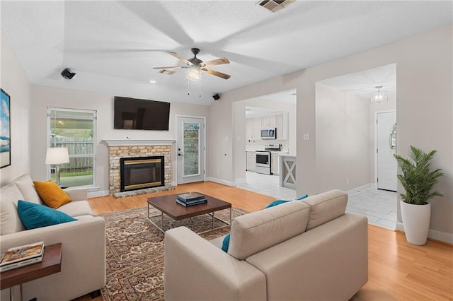 living room featuring ceiling fan, a healthy amount of sunlight, a fireplace, and light hardwood / wood-style flooring