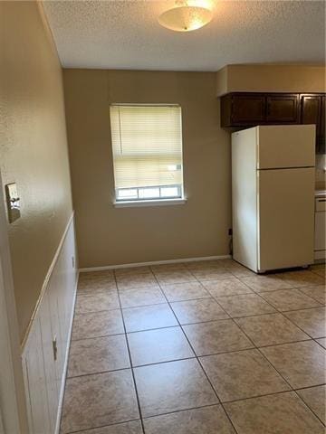 kitchen with a textured ceiling, light tile patterned floors, white refrigerator, and dark brown cabinets