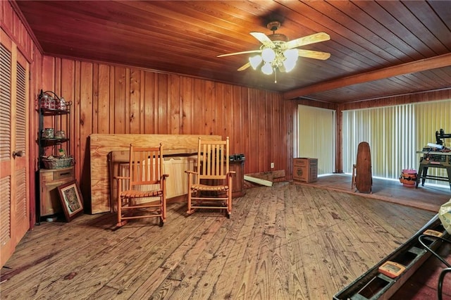 living area with ceiling fan, wooden ceiling, and wood walls