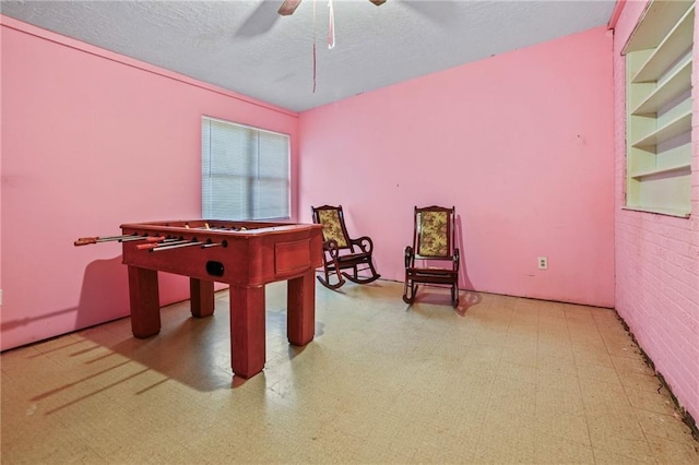 recreation room with ceiling fan and brick wall