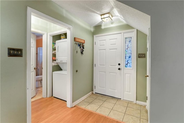 tiled foyer entrance with stacked washer and dryer and a textured ceiling