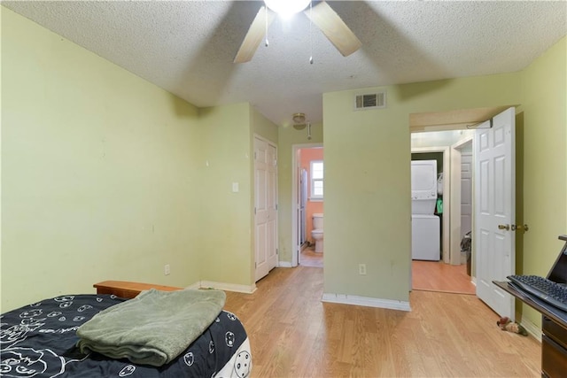 bedroom with ceiling fan, stacked washer / drying machine, ensuite bath, light hardwood / wood-style flooring, and a textured ceiling