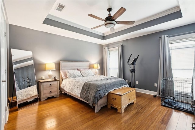 bedroom with ceiling fan, ornamental molding, hardwood / wood-style flooring, and a tray ceiling