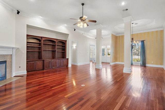 unfurnished living room with a tile fireplace, ceiling fan with notable chandelier, ornamental molding, and decorative columns