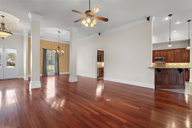 unfurnished living room with ornate columns, dark hardwood / wood-style flooring, crown molding, and ceiling fan with notable chandelier