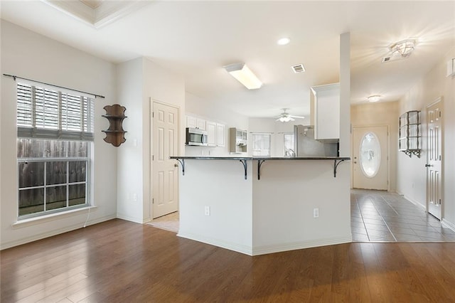 kitchen with hardwood / wood-style flooring, kitchen peninsula, stainless steel appliances, a kitchen breakfast bar, and white cabinets