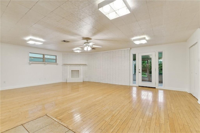 unfurnished living room with ceiling fan, brick wall, a brick fireplace, and light wood-type flooring