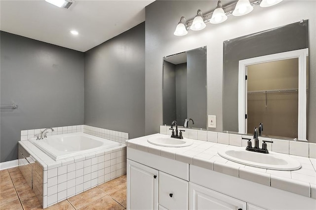 bathroom with tiled bath, vanity, and tile patterned flooring