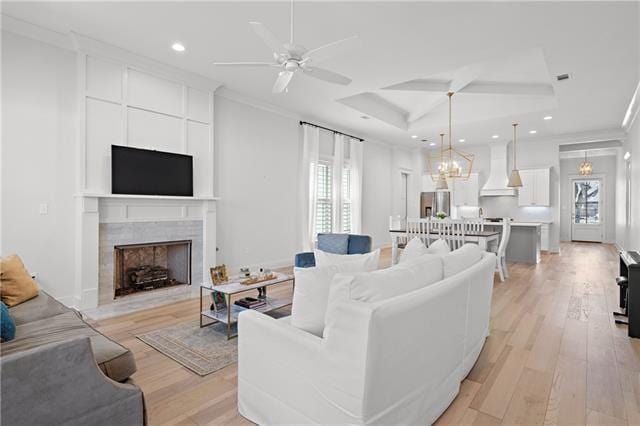 living room with ceiling fan, a tiled fireplace, a raised ceiling, crown molding, and light hardwood / wood-style flooring