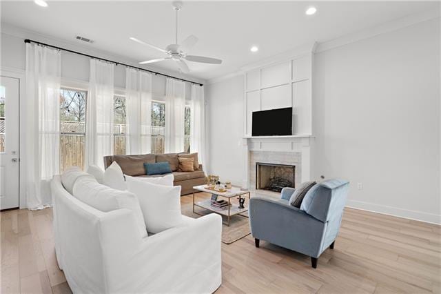 living room with ceiling fan, light wood-type flooring, a large fireplace, and ornamental molding