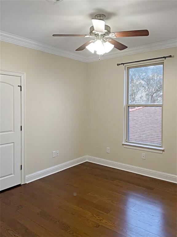 empty room with dark wood-type flooring, crown molding, and ceiling fan