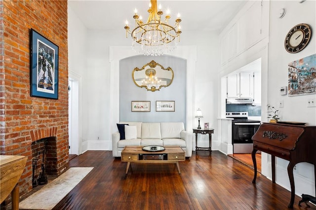 living room with a towering ceiling, a brick fireplace, hardwood / wood-style floors, and an inviting chandelier