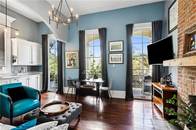 living area featuring a fireplace, a healthy amount of sunlight, a chandelier, and dark hardwood / wood-style flooring