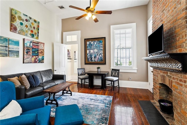 living room featuring a brick fireplace, dark wood-type flooring, and ceiling fan