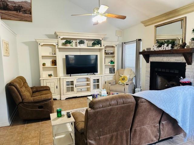 living room featuring a brick fireplace, lofted ceiling, ceiling fan, and light tile patterned flooring