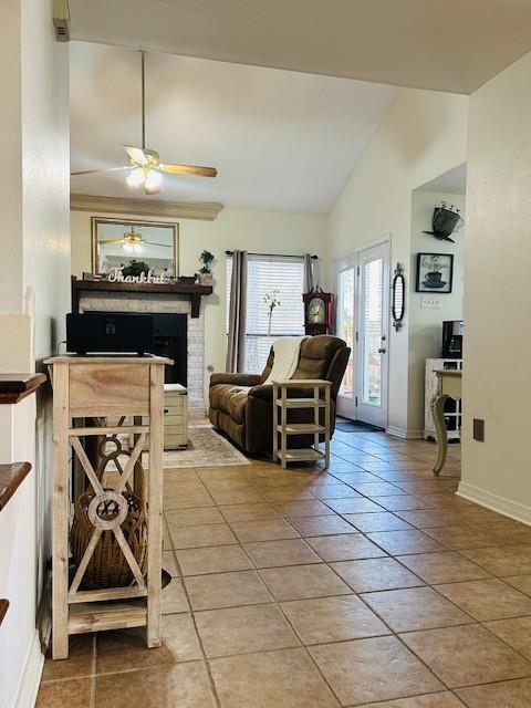 living room featuring vaulted ceiling, ceiling fan, tile patterned floors, and a brick fireplace