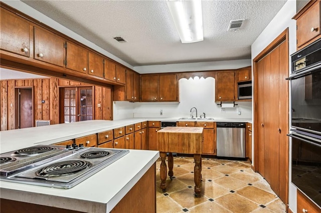 kitchen with kitchen peninsula, sink, appliances with stainless steel finishes, a textured ceiling, and french doors