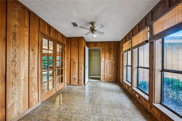 empty room featuring ceiling fan, a textured ceiling, french doors, and wooden walls