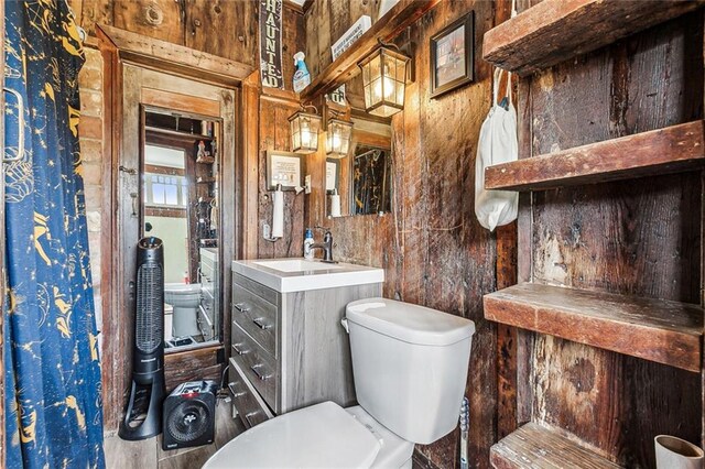 bathroom featuring toilet, vanity, and wooden walls