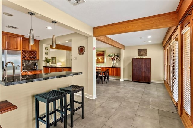 kitchen with kitchen peninsula, stainless steel fridge, hanging light fixtures, a breakfast bar, and beamed ceiling