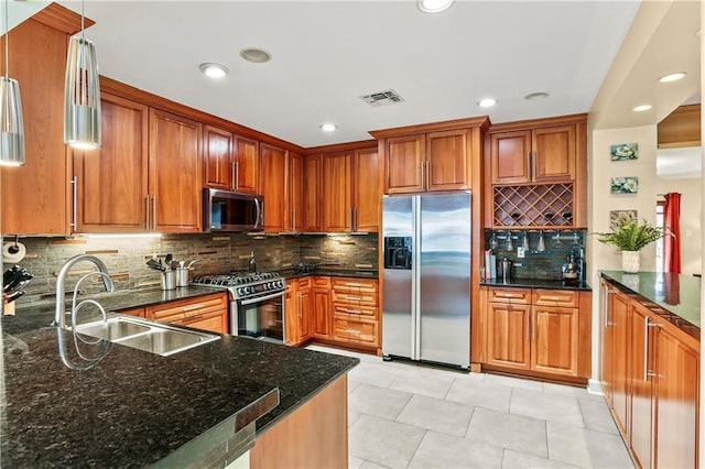 kitchen with light tile patterned floors, appliances with stainless steel finishes, dark stone countertops, hanging light fixtures, and sink