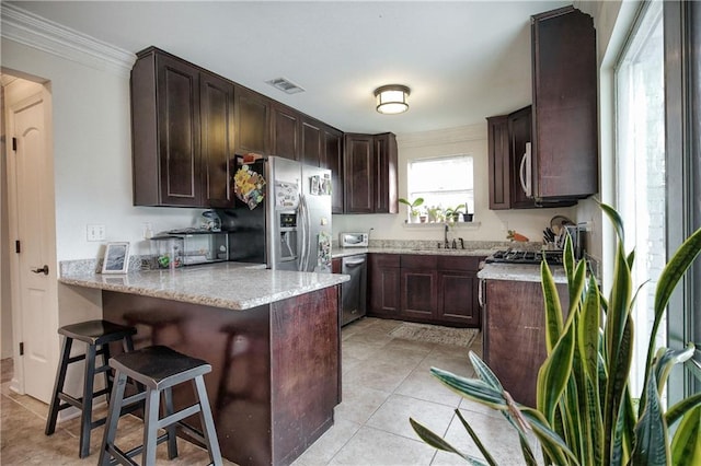 kitchen with kitchen peninsula, light stone countertops, appliances with stainless steel finishes, ornamental molding, and dark brown cabinets