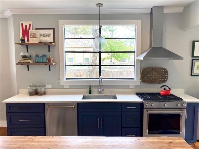 kitchen featuring blue cabinets, sink, hanging light fixtures, stainless steel appliances, and wall chimney range hood