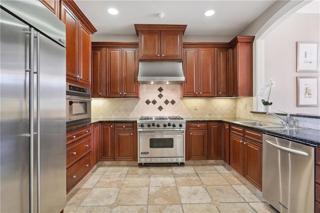 kitchen with range hood, dark stone countertops, a sink, decorative backsplash, and premium appliances