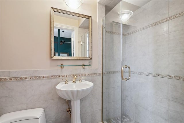 bathroom with a shower stall, toilet, tile walls, and a sink
