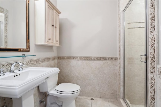 bathroom featuring tile patterned flooring, a shower with door, sink, tile walls, and toilet