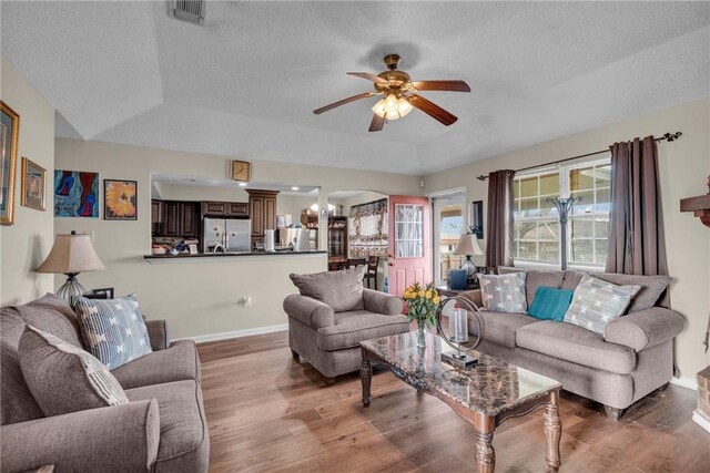 living room with a textured ceiling, ceiling fan with notable chandelier, hardwood / wood-style floors, and a tray ceiling