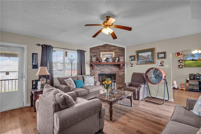 living room with light hardwood / wood-style floors, ceiling fan, lofted ceiling, a fireplace, and a textured ceiling