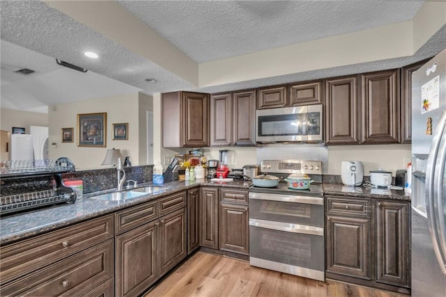 kitchen featuring a textured ceiling, appliances with stainless steel finishes, dark stone countertops, and sink