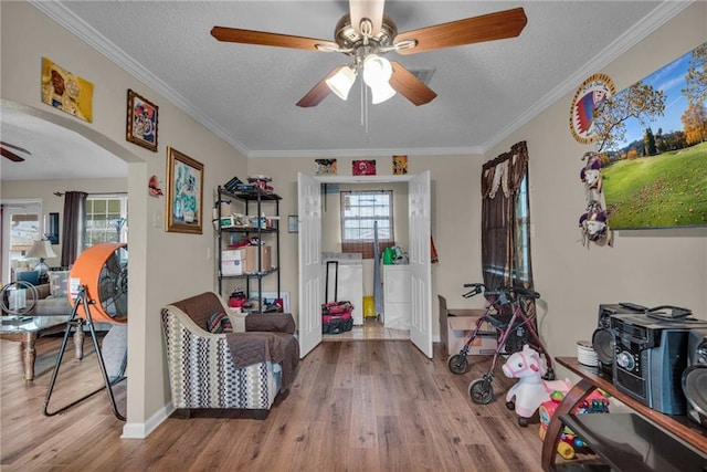 interior space with a textured ceiling, ceiling fan, crown molding, and light wood-type flooring