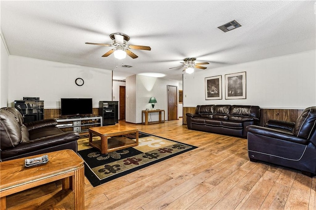 living room with ceiling fan, a textured ceiling, light hardwood / wood-style flooring, and wooden walls