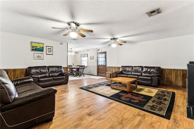 living room with a textured ceiling, ceiling fan, and light hardwood / wood-style flooring