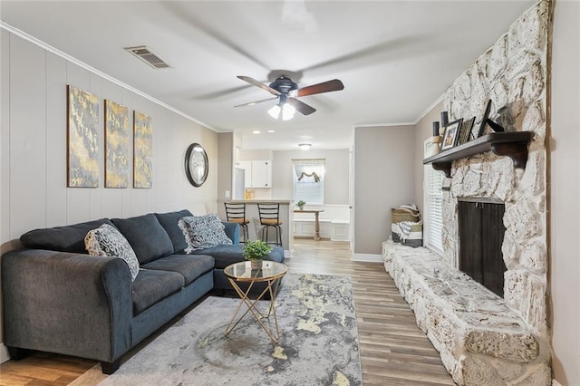 living room with hardwood / wood-style floors, crown molding, a stone fireplace, and ceiling fan