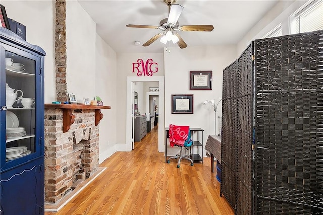 office space with ceiling fan, a brick fireplace, and light wood-type flooring