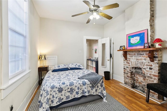 bedroom featuring ceiling fan, hardwood / wood-style floors, and a brick fireplace