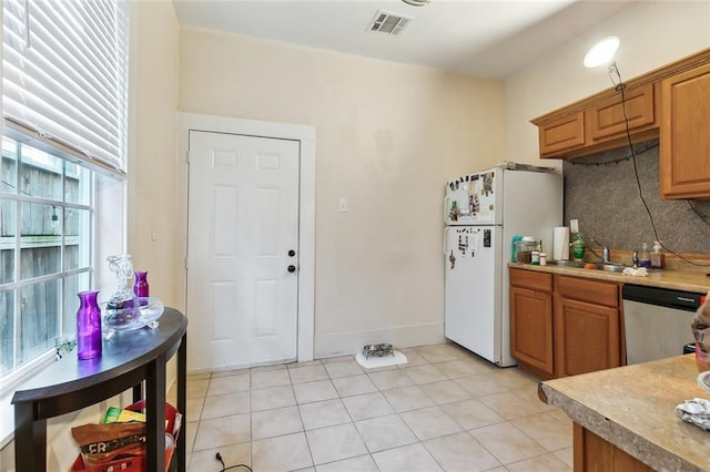 kitchen featuring light tile patterned floors, tasteful backsplash, white refrigerator, stainless steel dishwasher, and sink