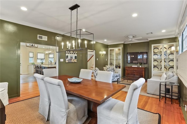 dining space with light wood-type flooring, crown molding, ceiling fan with notable chandelier, and sink