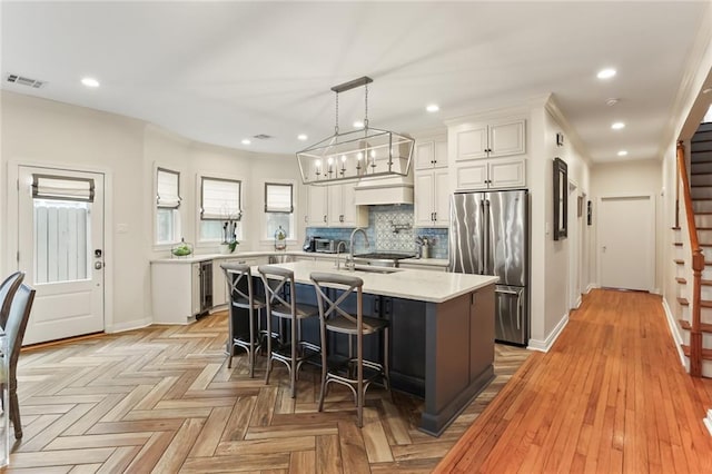 kitchen with white cabinets, decorative light fixtures, an island with sink, high end refrigerator, and a breakfast bar area