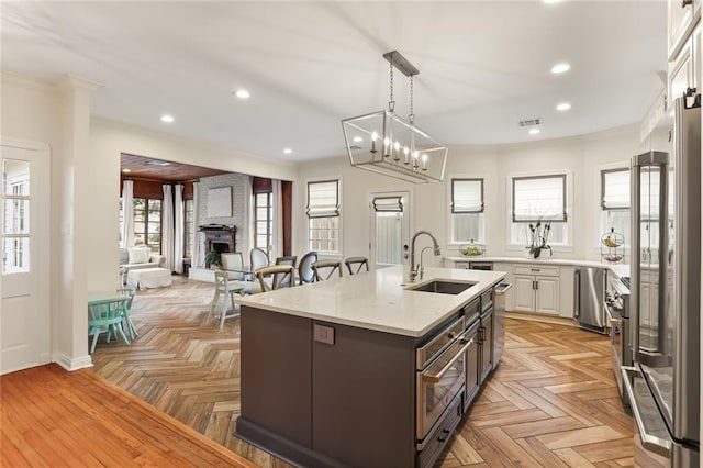 kitchen with white cabinetry, a center island with sink, high end fridge, light parquet flooring, and sink