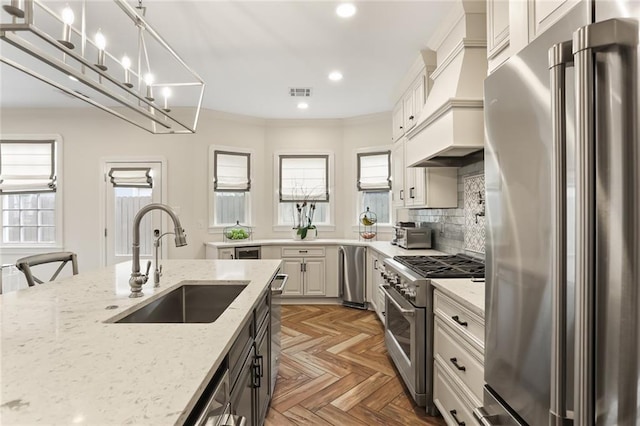 kitchen featuring premium appliances, sink, hanging light fixtures, light stone counters, and custom range hood