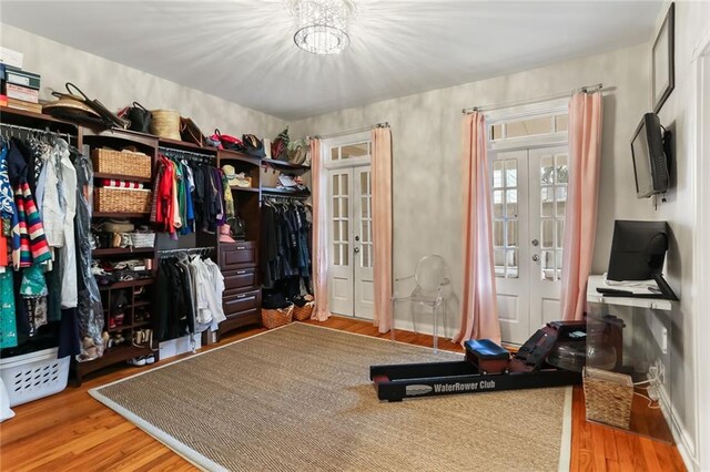 walk in closet with french doors, an inviting chandelier, and wood-type flooring